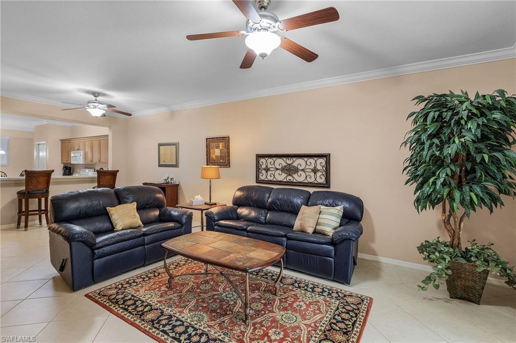 Spacious living area featuring tile flooring, ceiling fans, and a partial wall opening to a kitchen bar with light wood cabinetry and a double sink