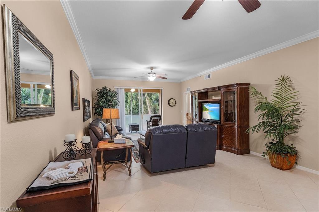 Spacious living area featuring large format tile flooring, crown molding, and two ceiling fans