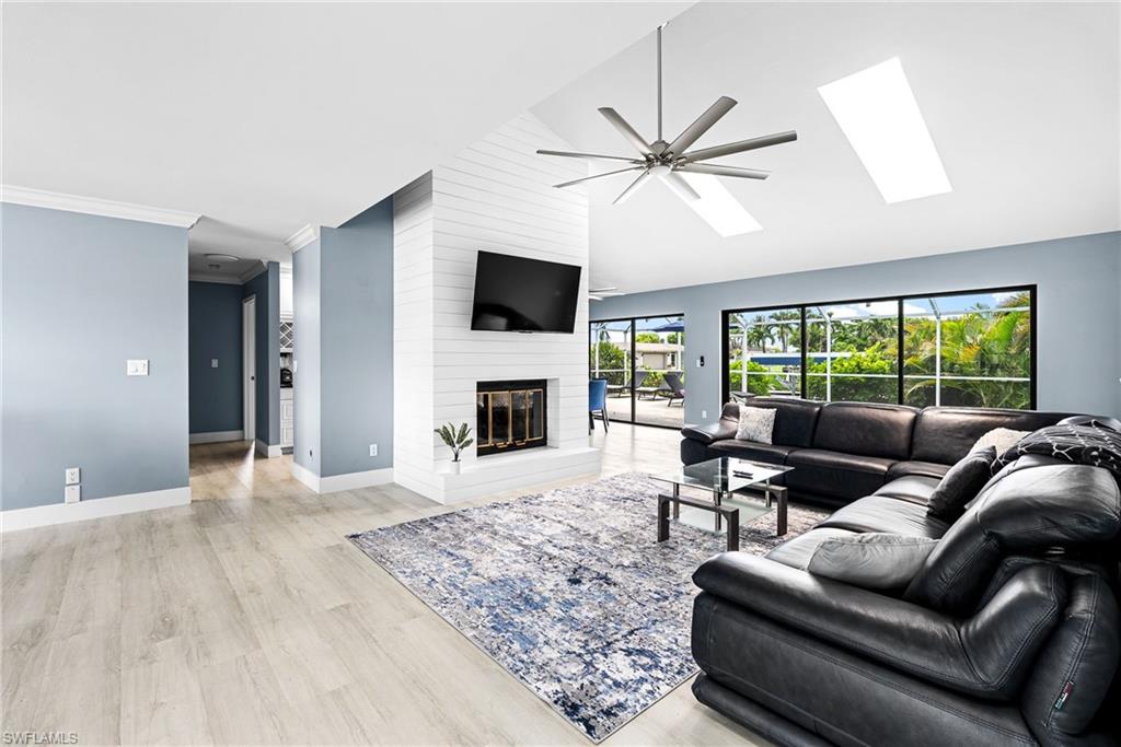 Living area with a fireplace, a ceiling fan, a skylight, light wood-type flooring, and crown molding
