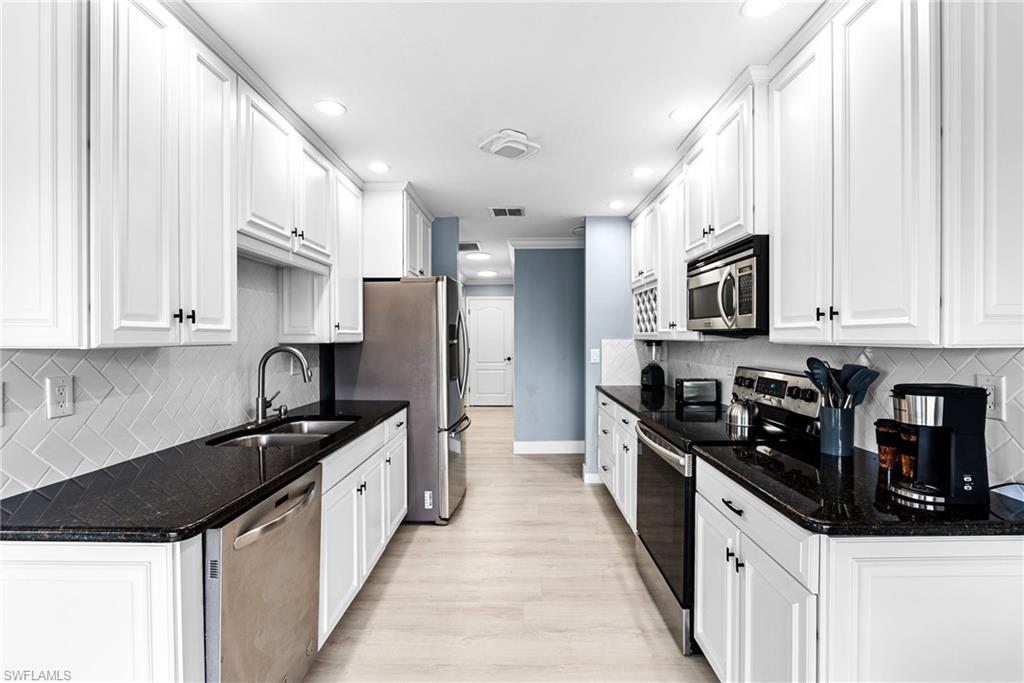 Kitchen with backsplash, appliances with stainless steel finishes, dark stone counters, white cabinetry, and light wood finished floors