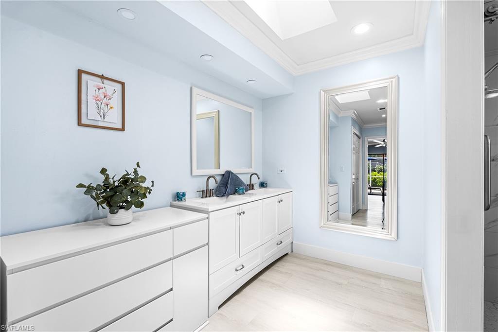 Full bathroom with ornamental molding, light wood-style floors, double vanity, a skylight, and recessed lighting