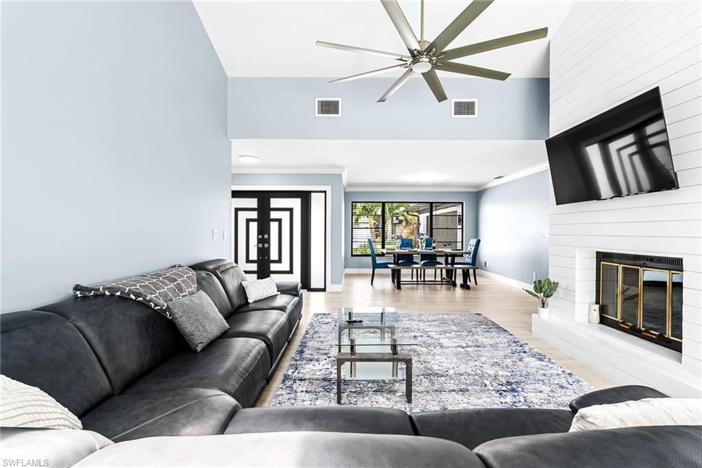 Living area featuring high vaulted ceiling, wood finished floors, a fireplace, crown molding, and a ceiling fan