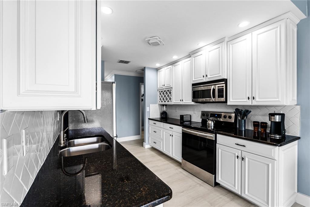 Kitchen with decorative backsplash, appliances with stainless steel finishes, white cabinets, dark stone countertops, and light wood-type flooring