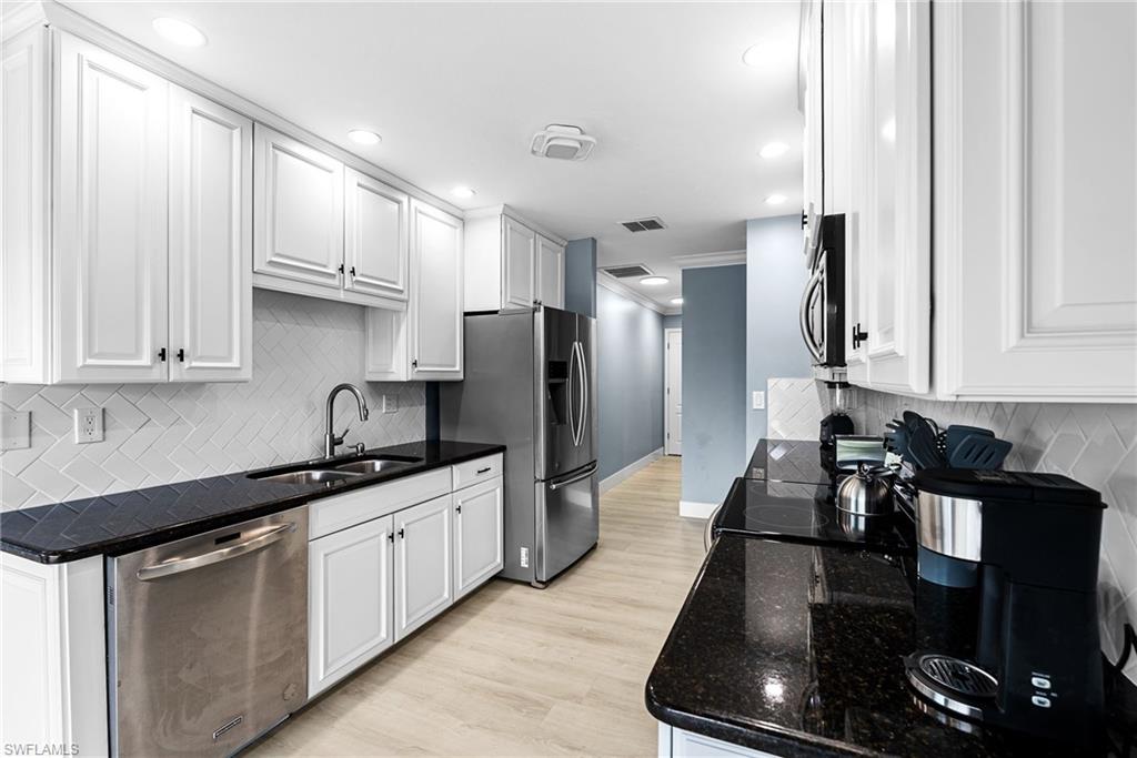 Kitchen featuring backsplash, stainless steel appliances, dark stone countertops, white cabinets, and recessed lighting