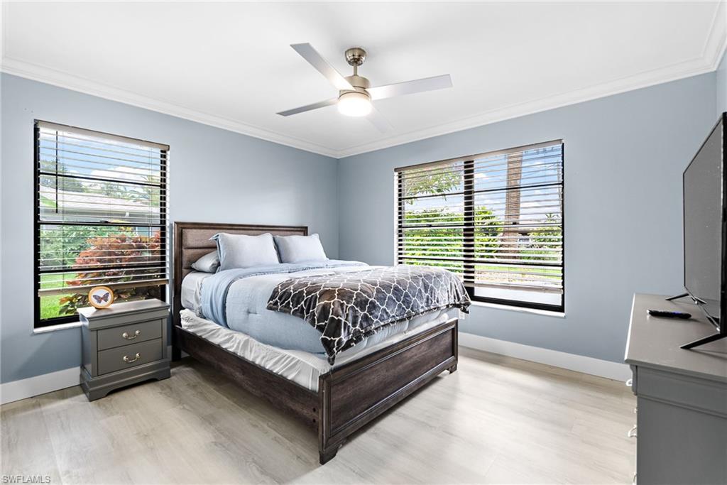 Bedroom with ornamental molding, multiple windows, light wood finished floors, and a ceiling fan