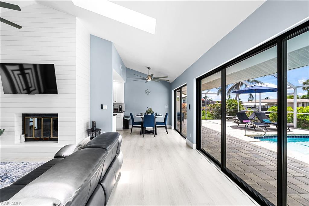 Living area with ceiling fan, light wood-type flooring, a skylight, a fireplace, and high vaulted ceiling