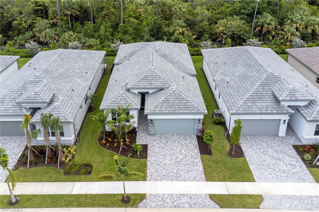 Modern residential property featuring a gray tile roof, paver driveway, manicured lawn, tropical landscaping, and an attached two-car garage
