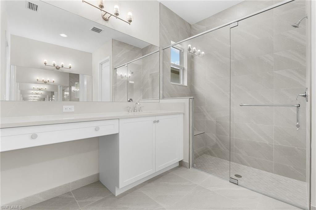 Primary bathroom featuring dual vanities with white cabinetry, quartz countertop, a large mirror, tile-to ceiling shower with seamless shower enclosure with 3/8" glass.