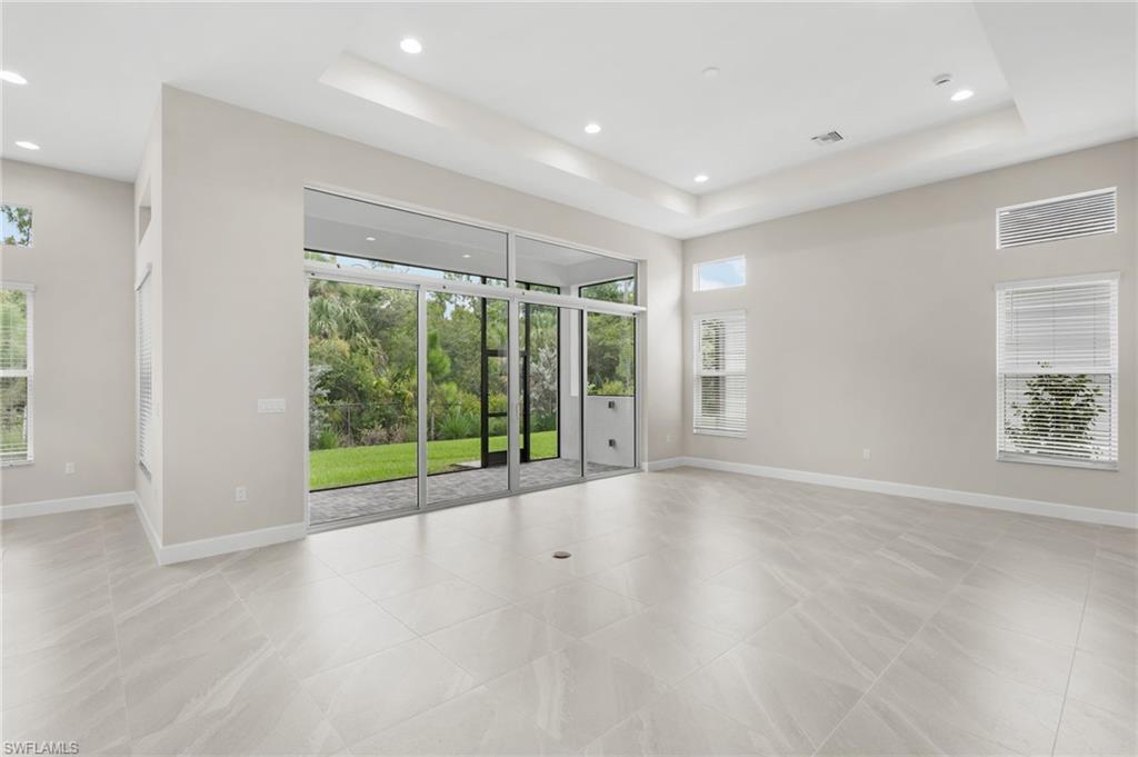 Spacious interior featuring large format porcelain 24'x24' tile flooring, a tray ceiling, recessed lighting, and expansive sliding glass doors opening to the covered lanai.