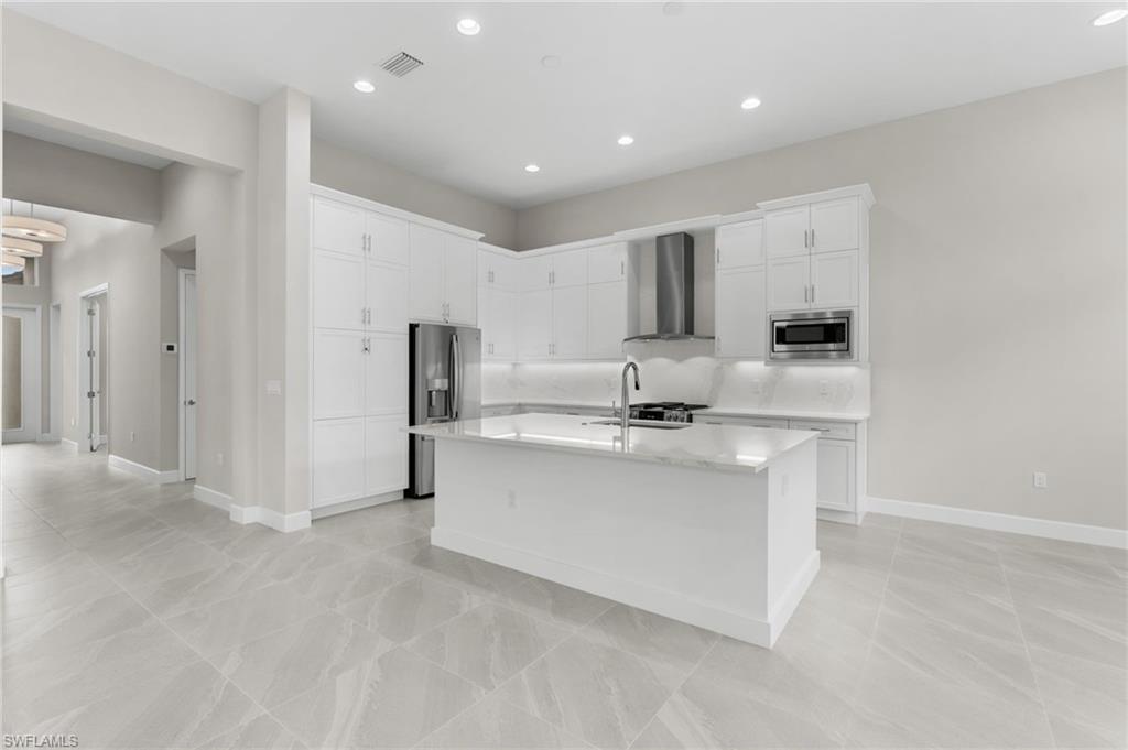 Modern kitchen featuring a central island, white shaker-style cabinetry, stainless steel appliances and vented hood, recessed lighting, premium quartz counters and backsplash.