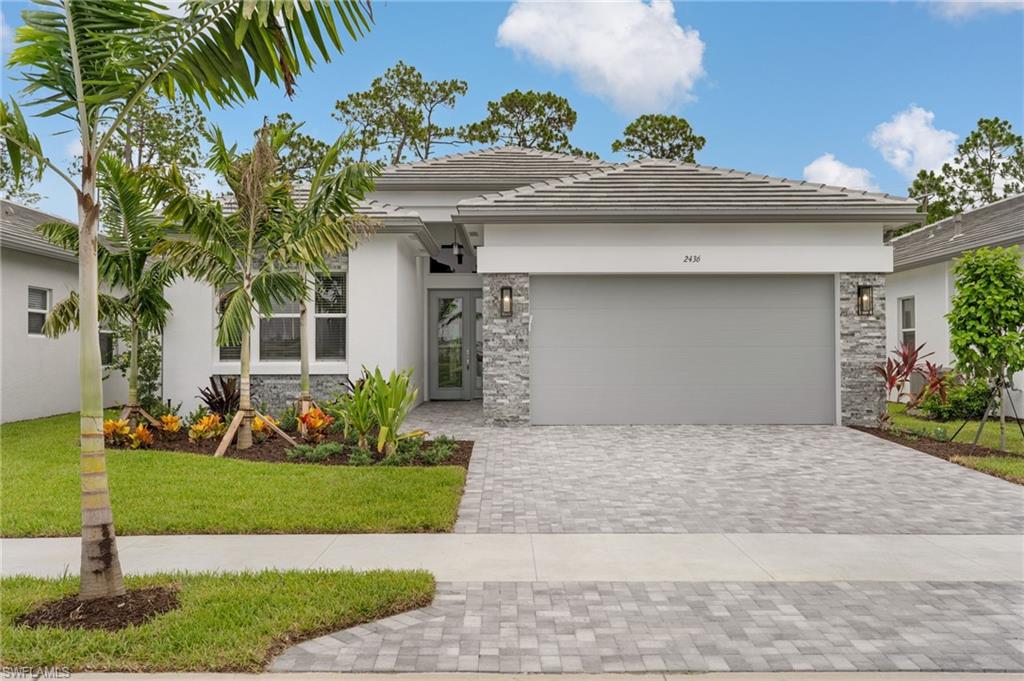 Newly introduced Stellar floorplan. Contemporary home exterior featuring a tile roof, stacked stone accents, paver driveway, and a landscaped entry with palm trees