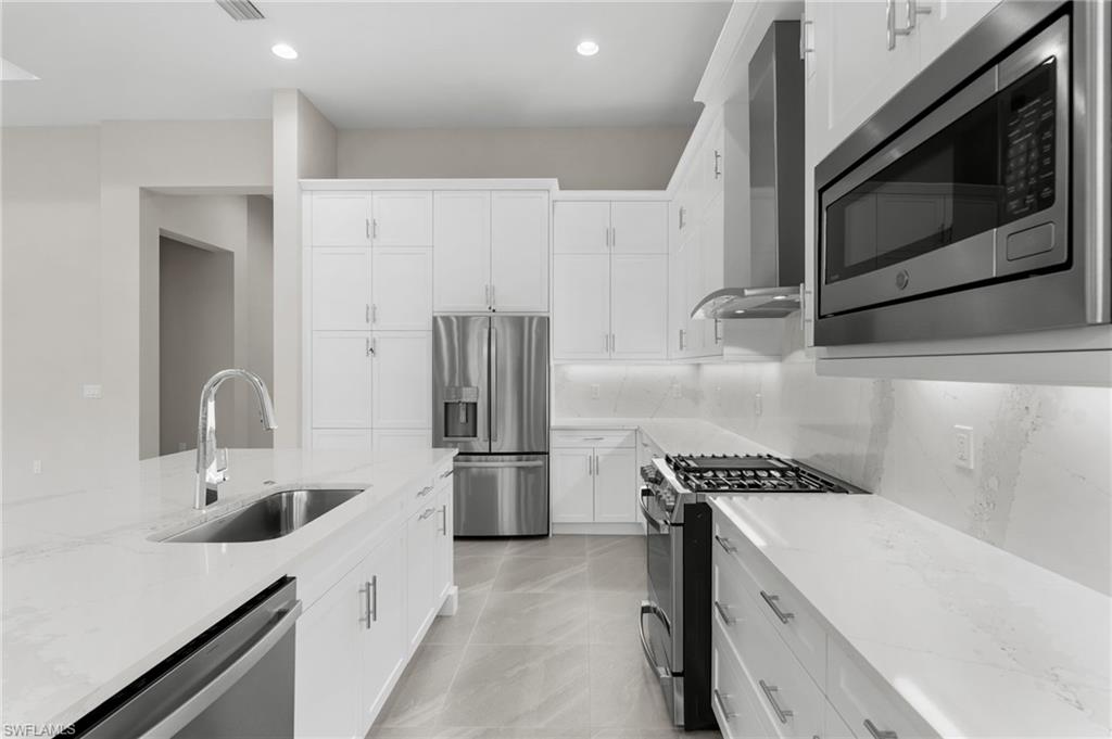 Modern kitchen featuring white cabinetry, light-premium quartz countertops & backsplash, and stainless steel appliances with vented hood.