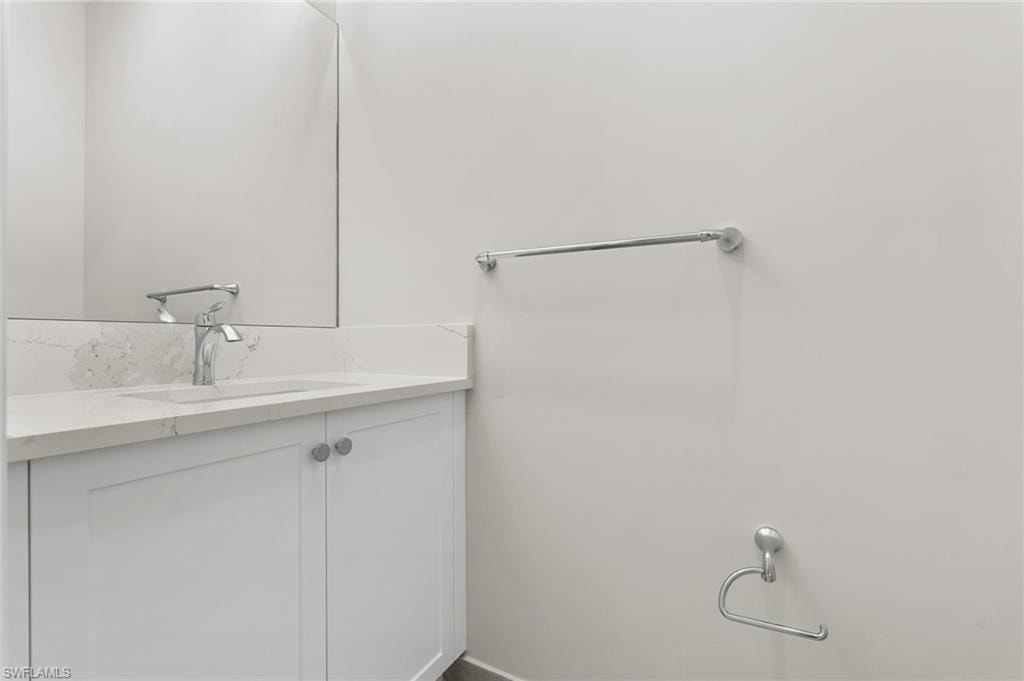 Guest powder room vanity featuring a quartz countertop with an integrated sink, polished chrome faucet, and white Shaker-style cabinetry with circular hardware