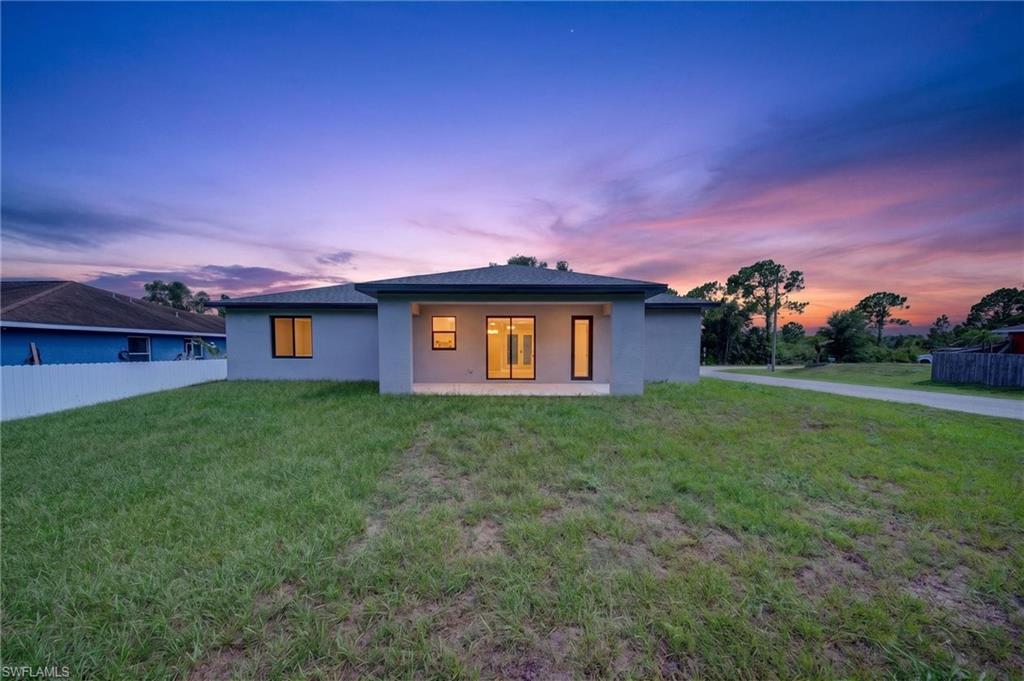Rear exterior featuring a covered patio, multiple windows, and a spacious grassy yard