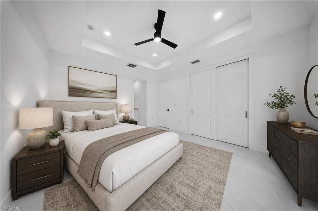 Recessed lighting illuminating a spacious room with a white tray ceiling and a black ceiling fan