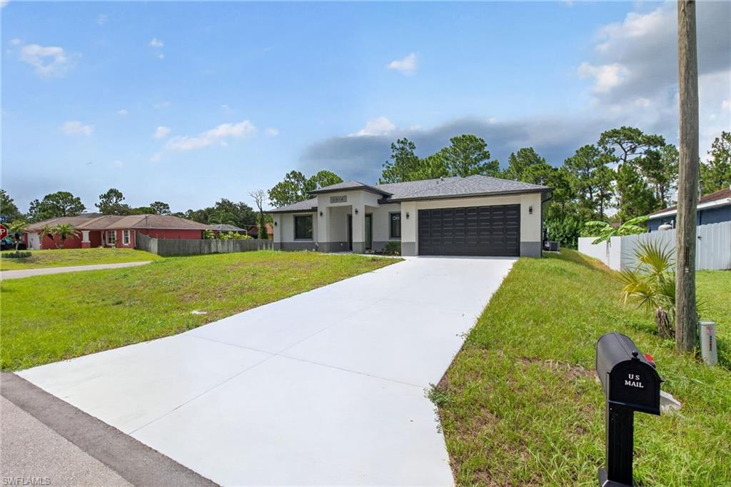 Contemporary stucco exterior featuring a covered entry, dark garage door, gray asphalt shingle roof, concrete driveway, and a spacious front yard