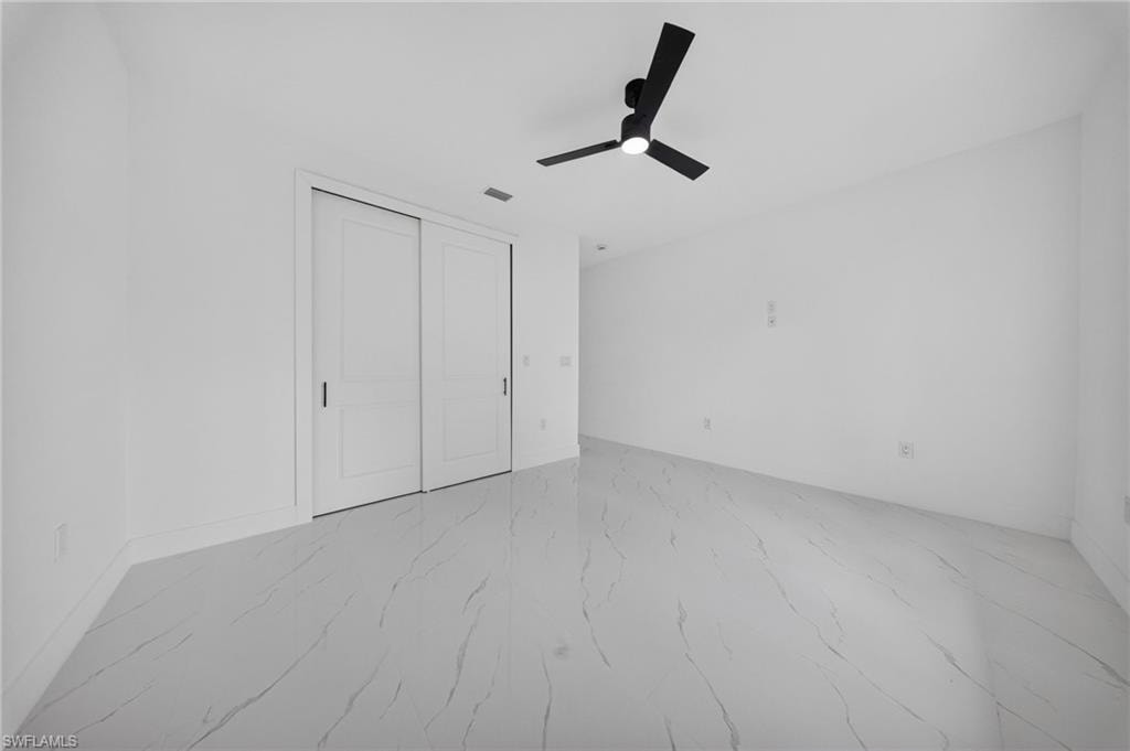 Spacious interior room featuring white walls, large format tile flooring, and a contemporary black ceiling fan