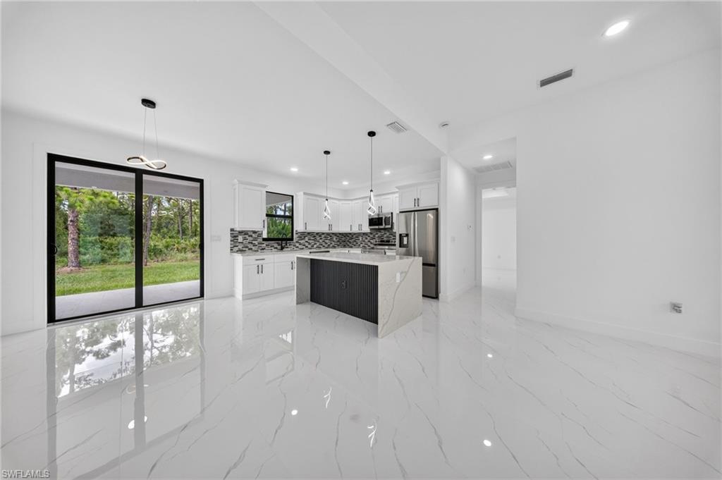 Open-concept interior featuring large format marble-look tile flooring, white shaker cabinetry, an island with a waterfall-edge countertop, stainless steel appliances, and sliding glass doors to the exterior