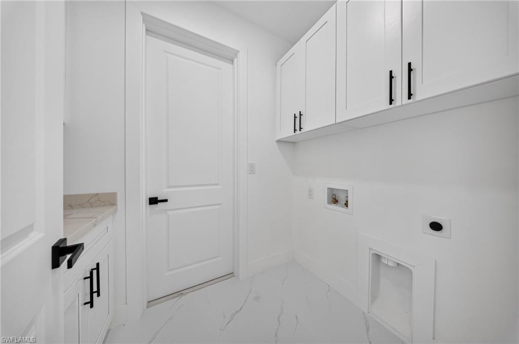 White laundry room featuring upper cabinetry with matte black hardware, a light-toned countertop, and white tile flooring