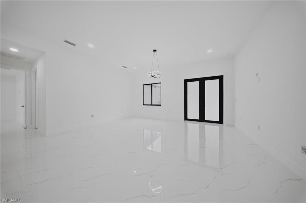 Spacious room featuring large format marble-look tile flooring, white walls, recessed lighting, and a contemporary chandelier