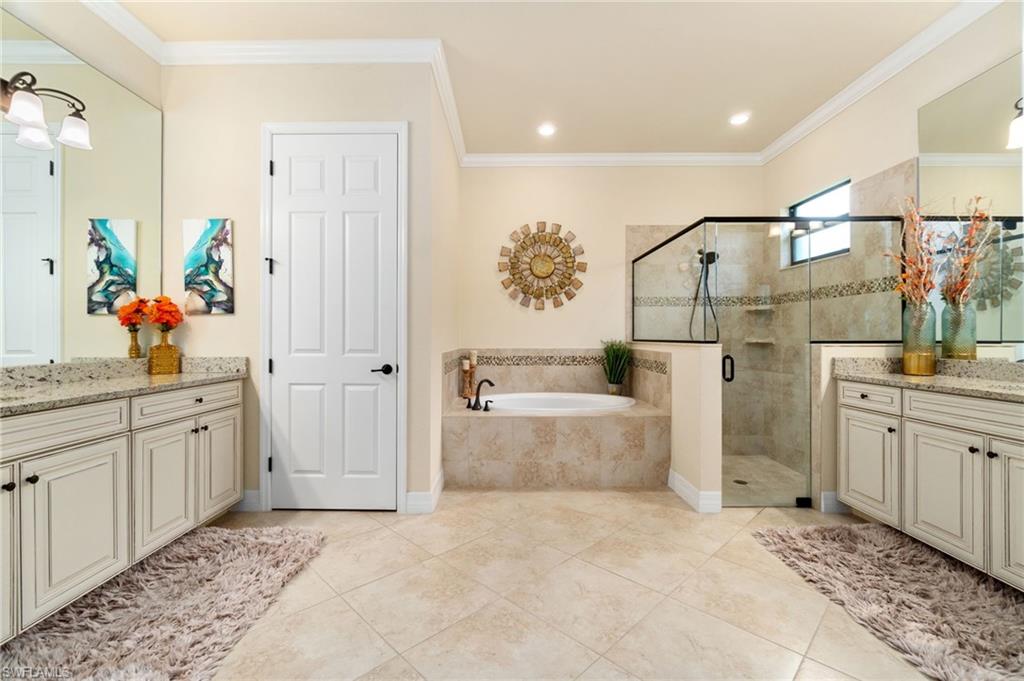 Spacious bathroom featuring a built-in soaking tub, a walk-in shower with glass enclosure, dual vanity sinks with light-toned countertops, and light-toned tile flooring