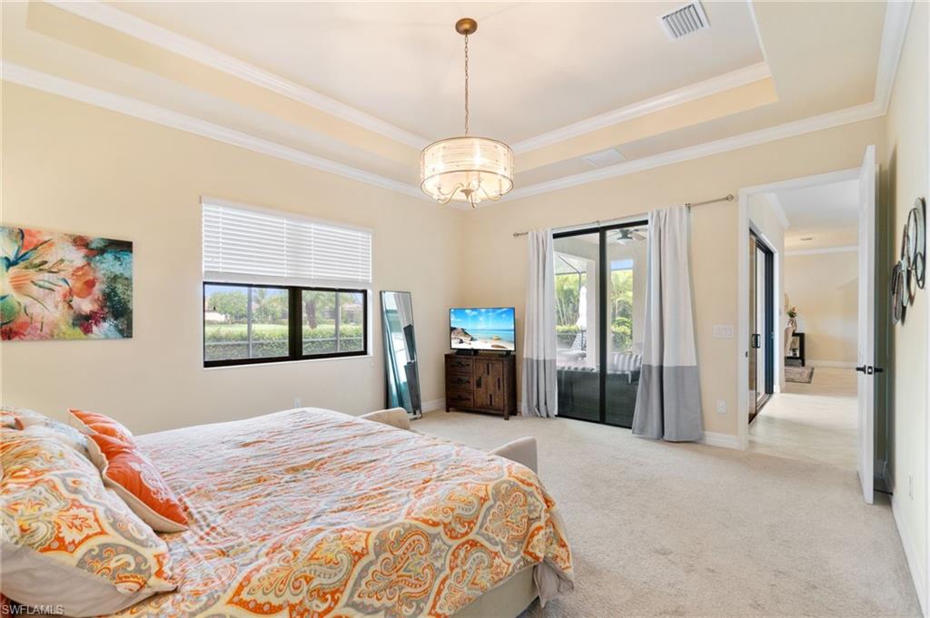 Carpeted room featuring a double tray ceiling with crown molding, a central chandelier, and a large window with blinds