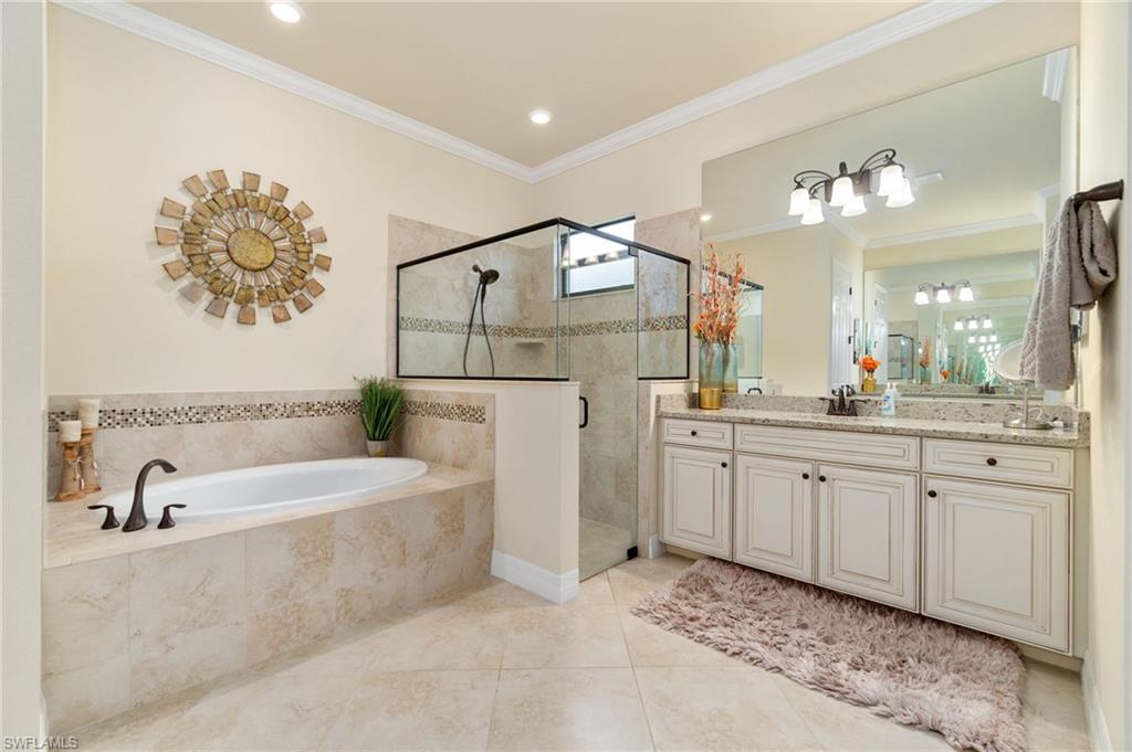 Bathroom featuring a built-in soaking tub, a frameless glass shower enclosure, a double vanity with stone-finish countertop, and tile flooring