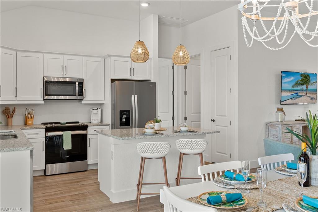 Kitchen with stainless steel appliances, light wood-style floors, white cabinets, hanging light fixtures, and a chandelier