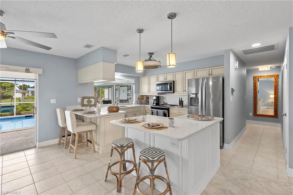 Kitchen with appliances with stainless steel finishes, a kitchen breakfast bar, light tile patterned floors, kitchen peninsula, and ceiling fan