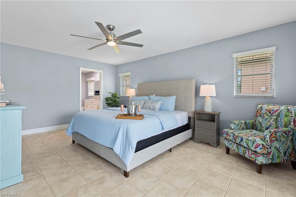 Bedroom with multiple windows, ensuite bathroom, light tile patterned flooring, and ceiling fan