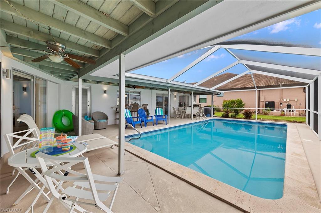 View of pool with glass enclosure, ceiling fan, and a patio