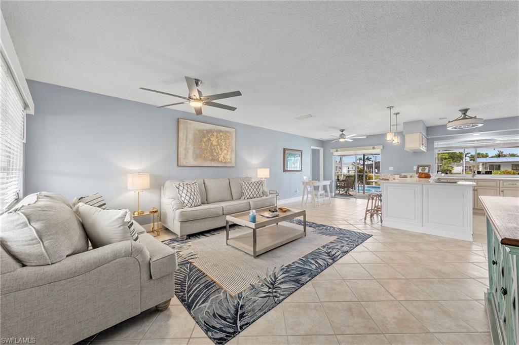 Living room with a textured ceiling, ceiling fan, and light tile patterned flooring