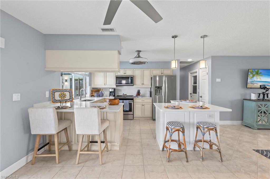 Kitchen with appliances with stainless steel finishes, light tile patterned flooring, cream cabinets, and a kitchen bar
