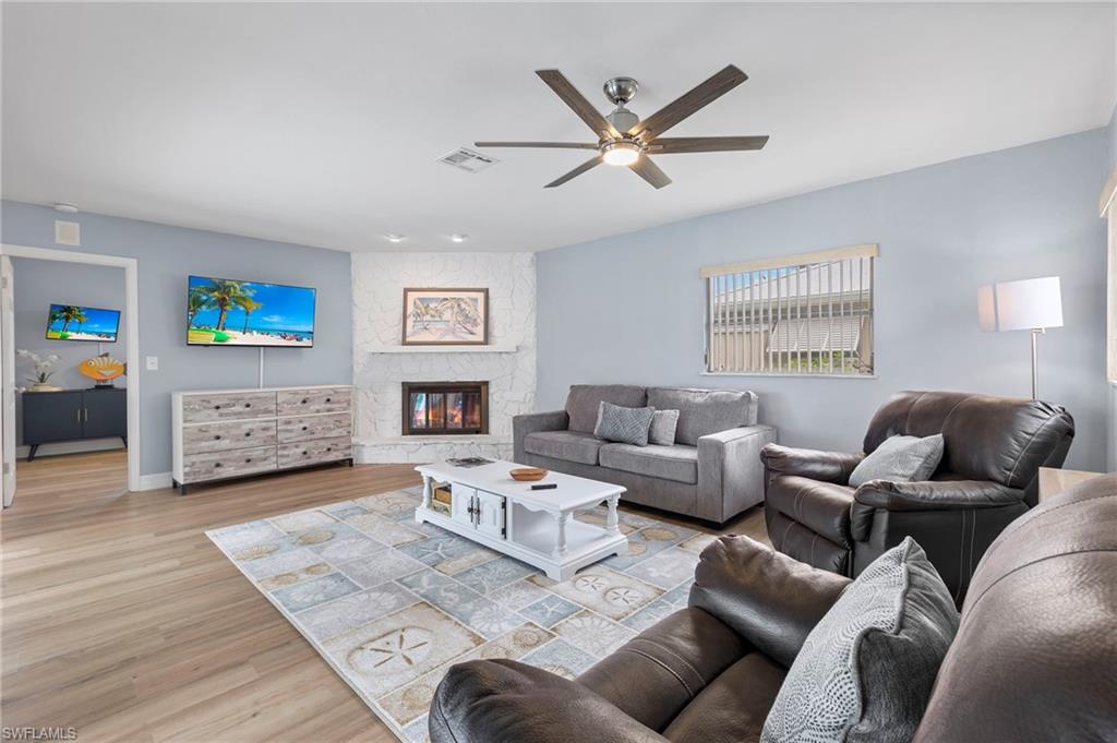 Living room featuring ceiling fan, light wood-type flooring, and a stone fireplace
