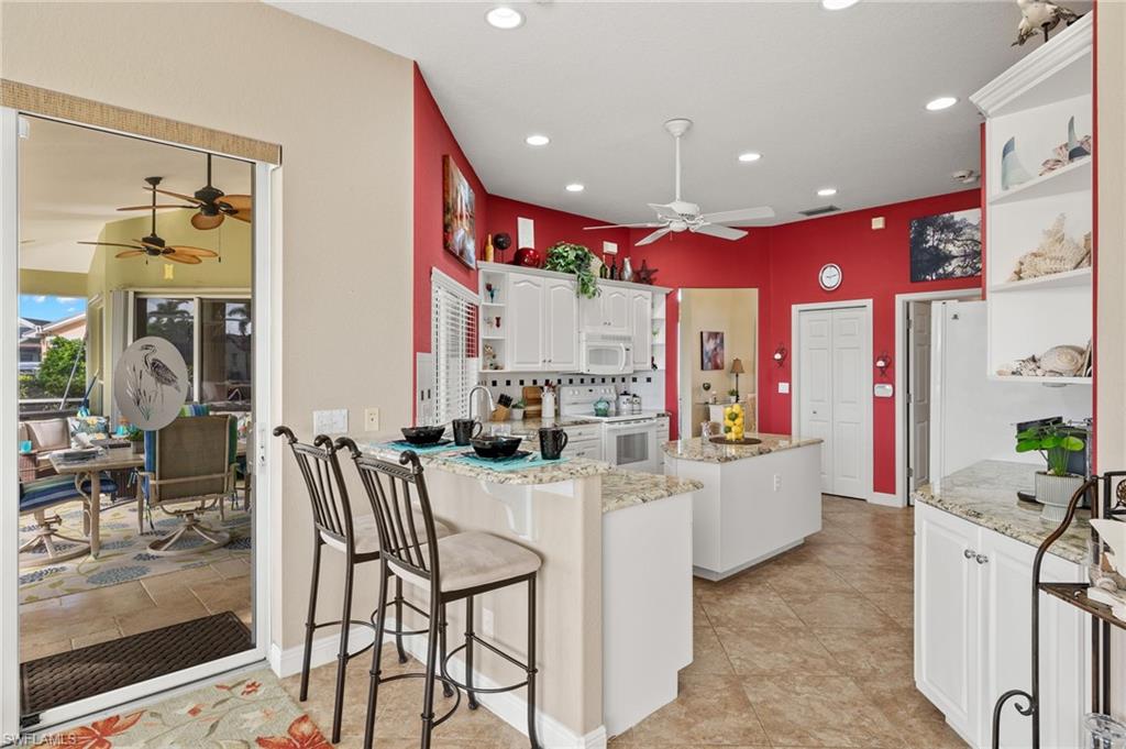 Kitchen with white appliances, white cabinets, light stone counters, decorative backsplash, and ceiling fan