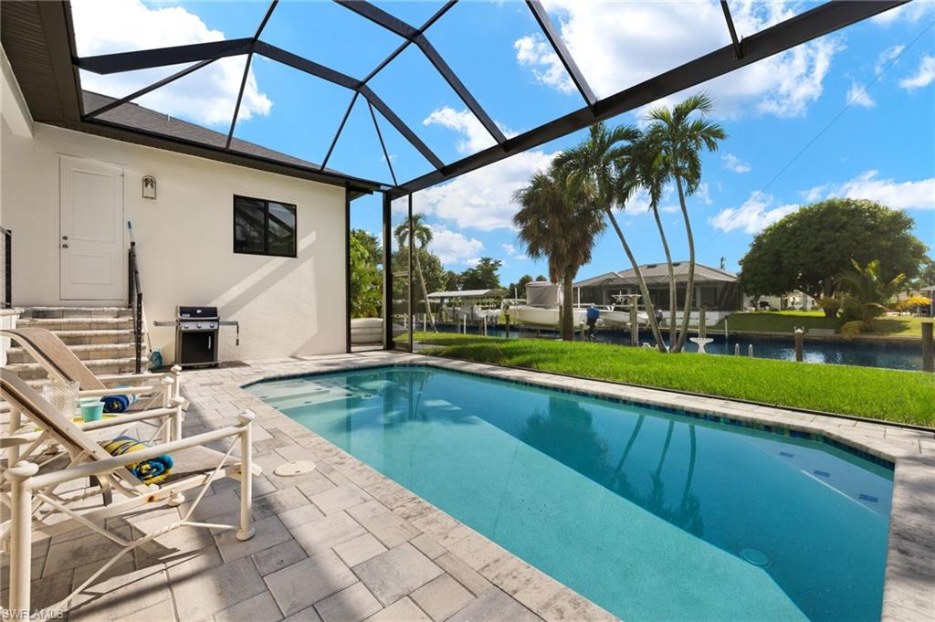 View of swimming pool with enclosure, a patio area, and a water view