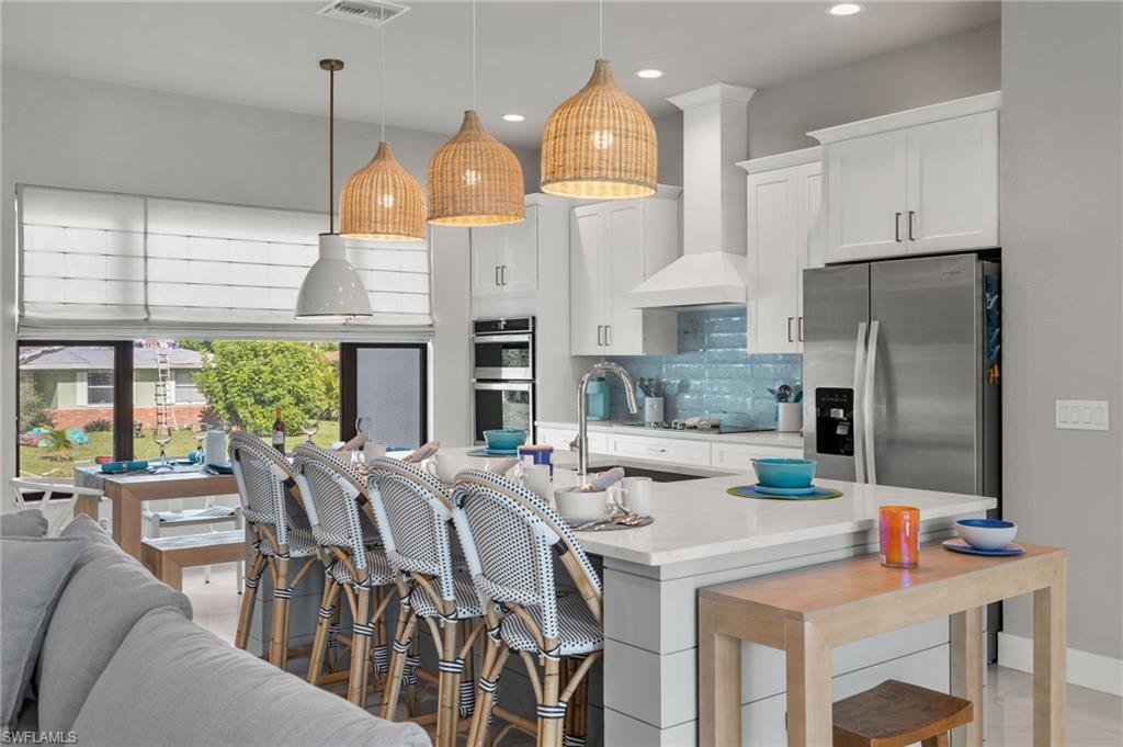 Kitchen featuring pendant lighting, stainless steel appliances, an island with sink, sink, and white cabinets