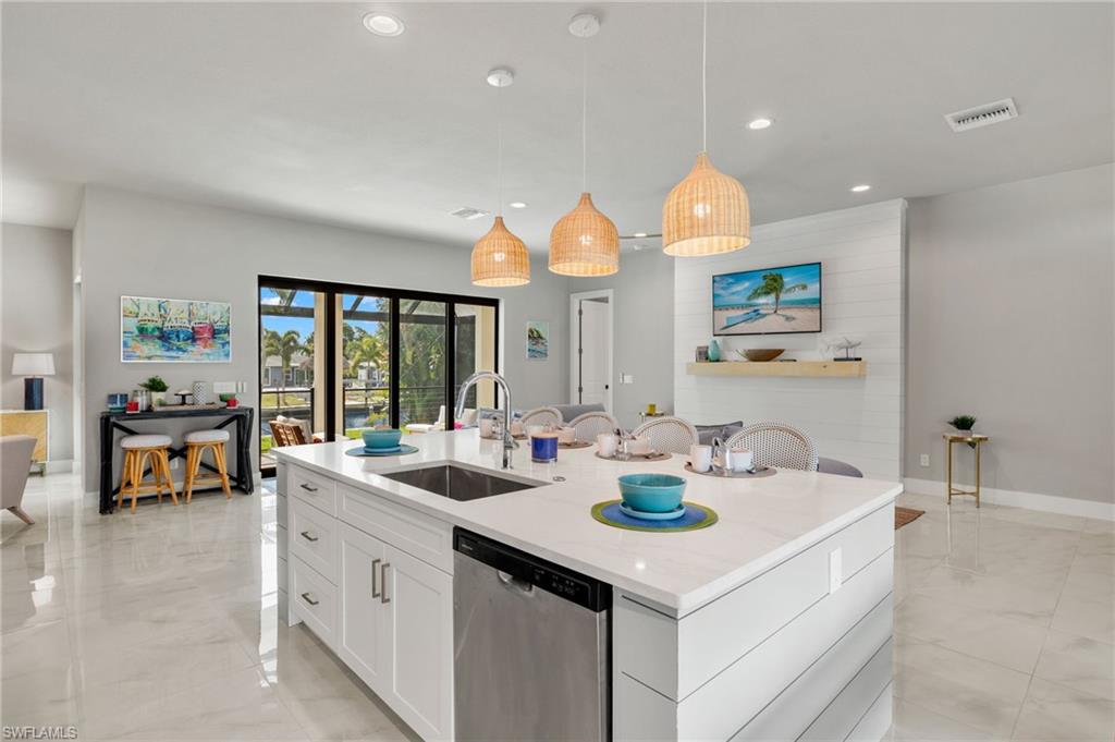 Kitchen with pendant lighting, a center island with sink, sink, stainless steel dishwasher, and white cabinets