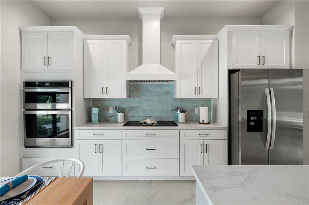 Kitchen featuring appliances with stainless steel finishes, tasteful backsplash, white cabinetry, light stone counters, and wall chimney range hood