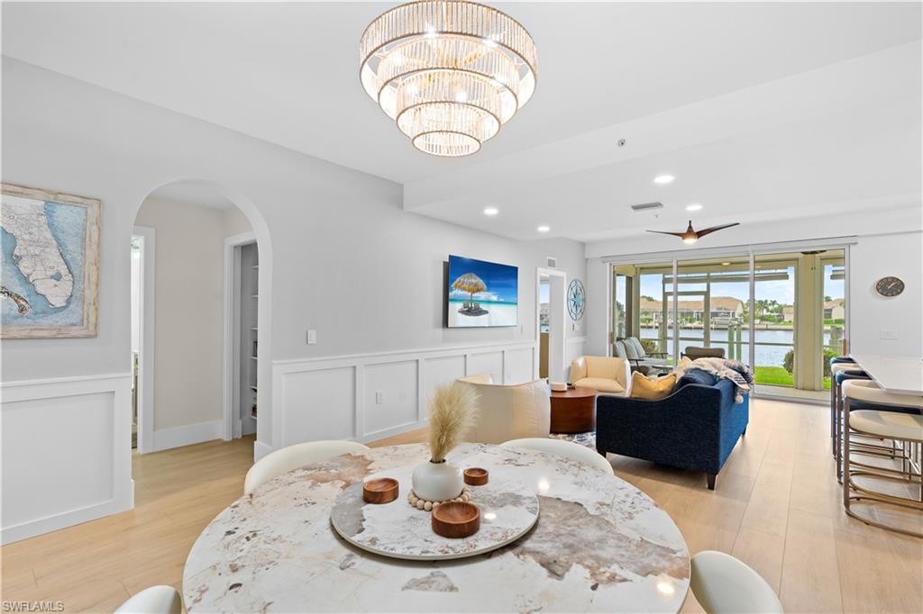 Open-concept living area with light wood-finish flooring, a tiered beaded chandelier, arched doorways, wainscoting, and large sliding glass doors opening to a water feature