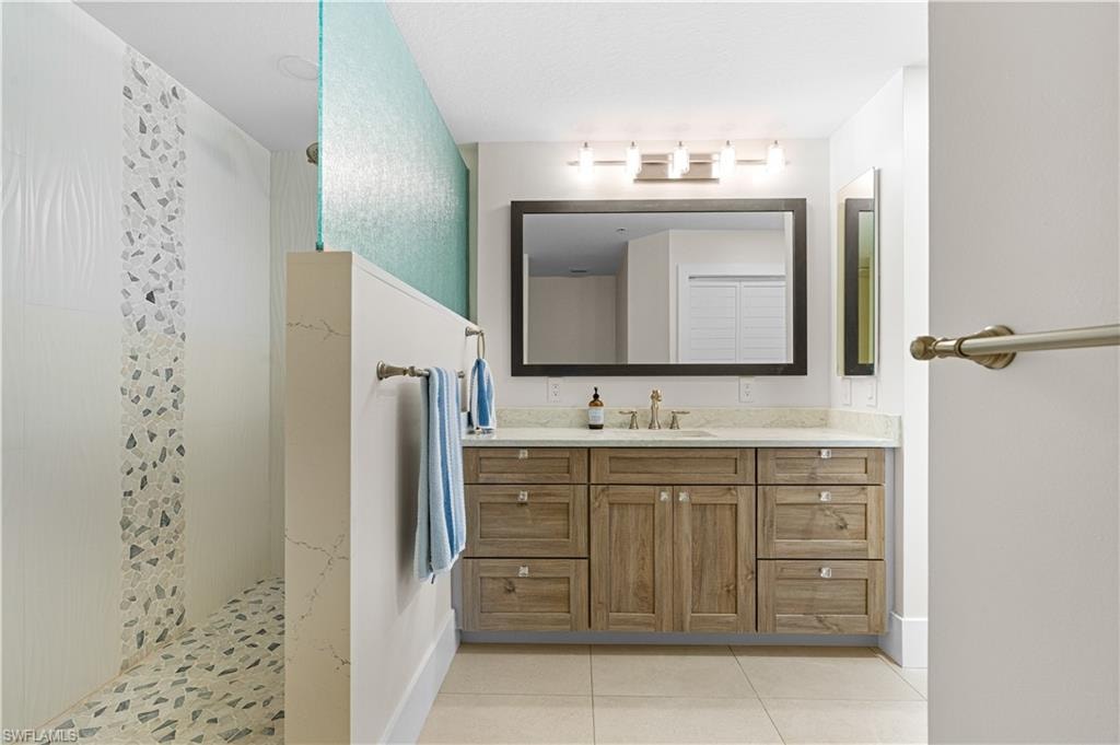 Bathroom featuring a wood-finish vanity with a single basin sink, white countertop, and a framed mirror
