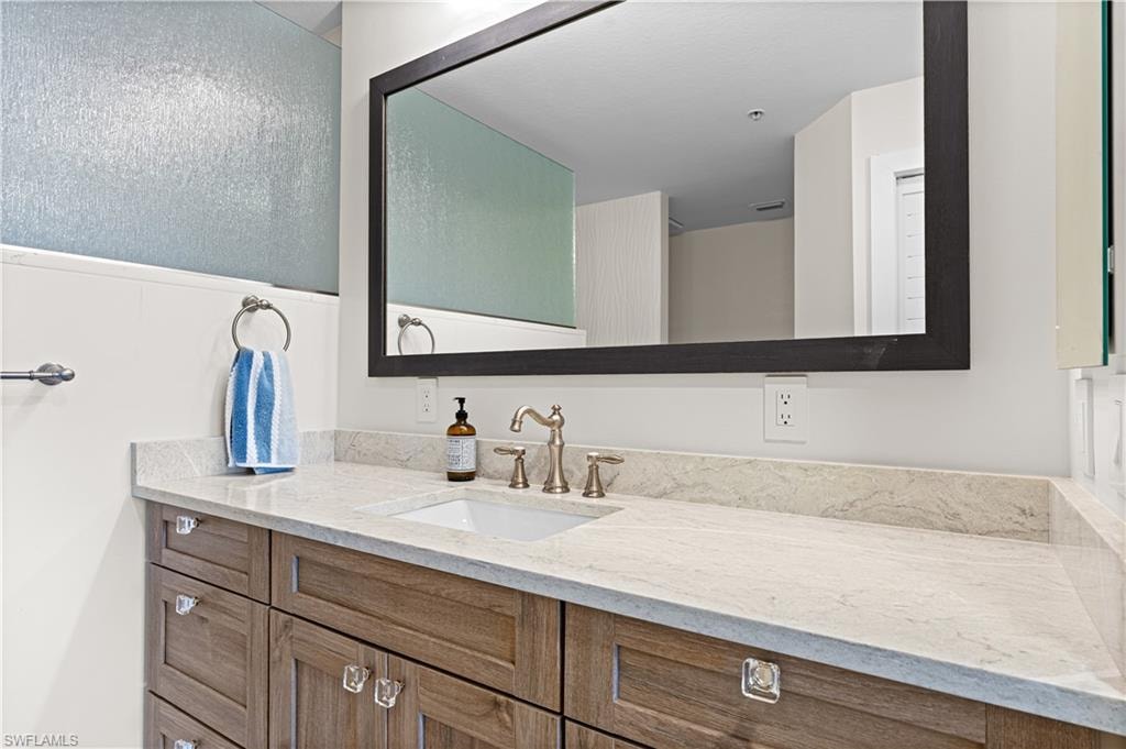 Vanity featuring wood-finish cabinetry, a light-toned countertop, and an undermount sink with a bronze-finish faucet