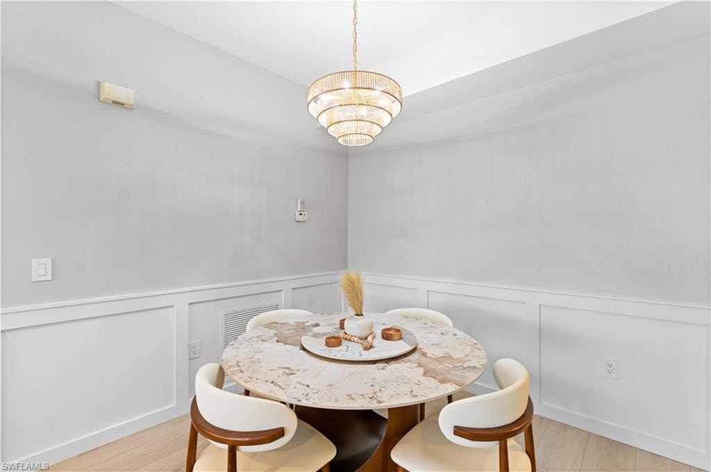 Dining area featuring a tiered chandelier, light wood-finish flooring, and wainscoting
