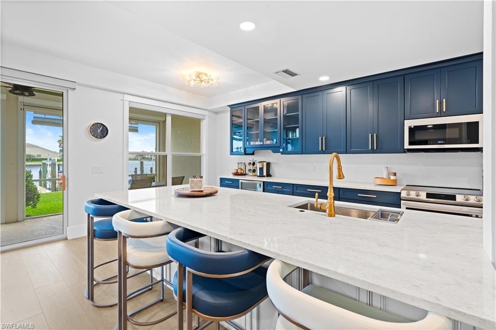 Kitchen featuring blue cabinetry, white countertops, a gold-toned faucet, stainless steel appliances, and wood-finish flooring