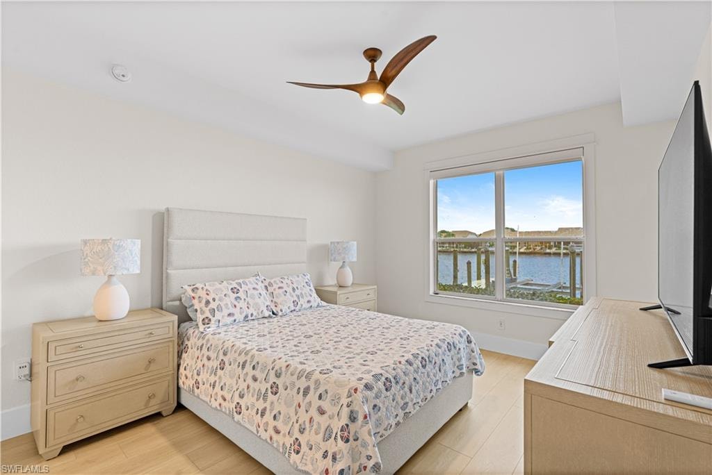 Light-filled room featuring a broad window with water scenery, wood-finish flooring, a ceiling fan, and a neutral color palette