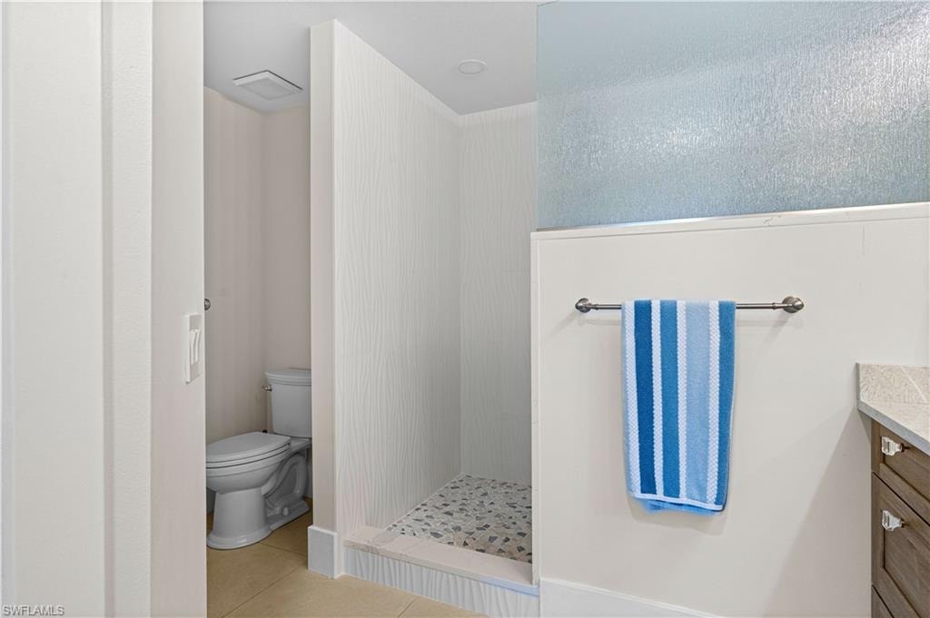 Bathroom featuring a walk-in shower with stone tile flooring, a separate water closet, and a vanity with a light-colored countertop
