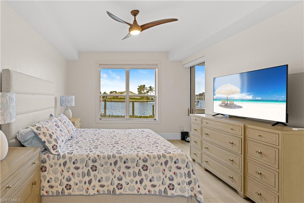 Bedroom featuring a waterside window, ceiling fan with integrated lighting, built-in dresser storage, and light-toned flooring