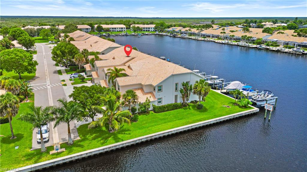 Waterfront property featuring a tile roof, mature palm trees, manicured lawn, and private boat docks