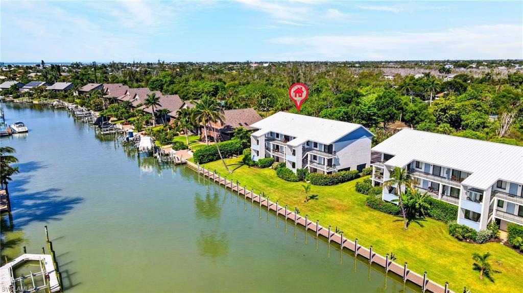 Waterfront residence featuring a private dock, lush green lawn, mature palm trees, and a multi-level architectural design