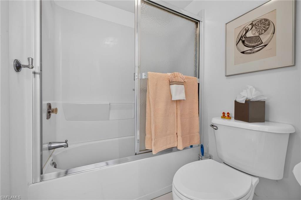 White bathroom featuring a built-in tub and shower combination with sliding glass doors, white walls, and a white toilet